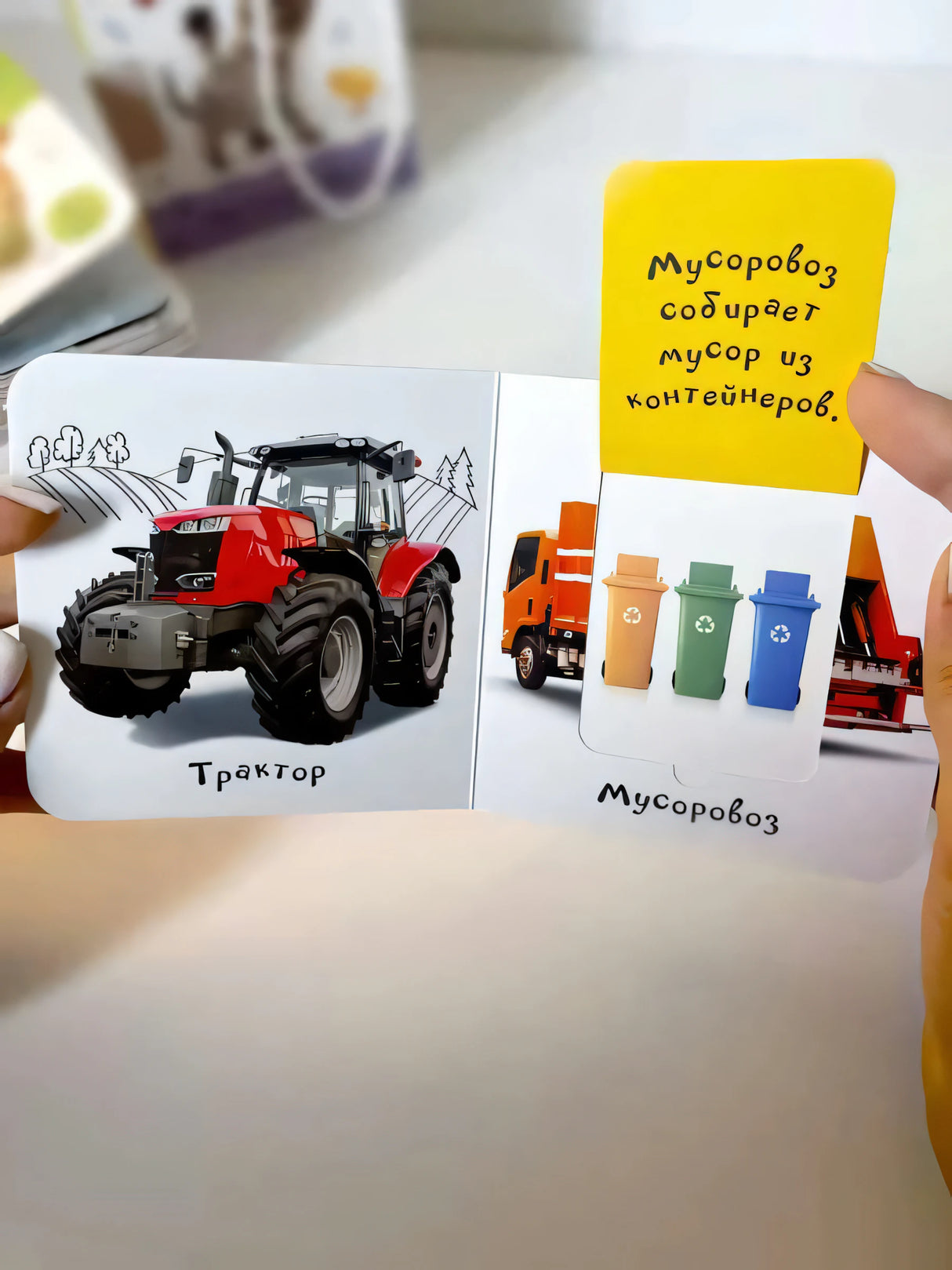 Книга «Машины» в руках: разворот «Трактор» и «Мусоровоз», клапан с текстом «Мусоровоз собирает мусор»