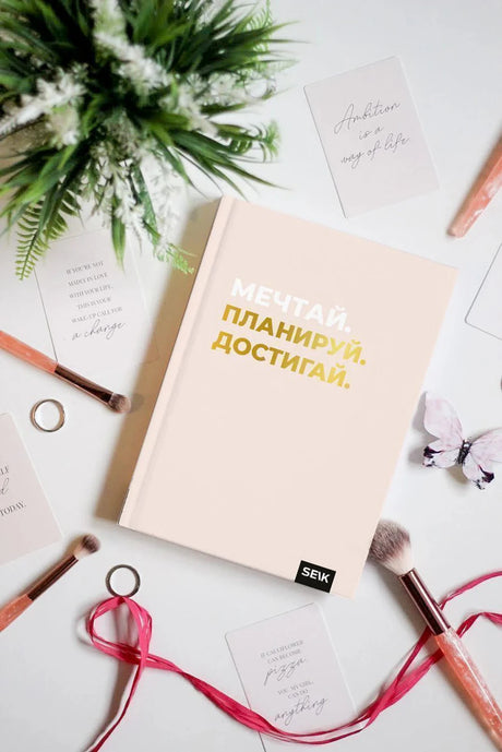 Розовый дневник «Мечтай. Планируй. Достигай.» среди цветов и канцелярии.
