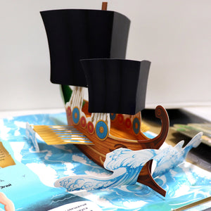 Раскрытый разворот книги с объёмным pop-up кораблём с чёрными парусами на фоне морских волн, текст об Эгее